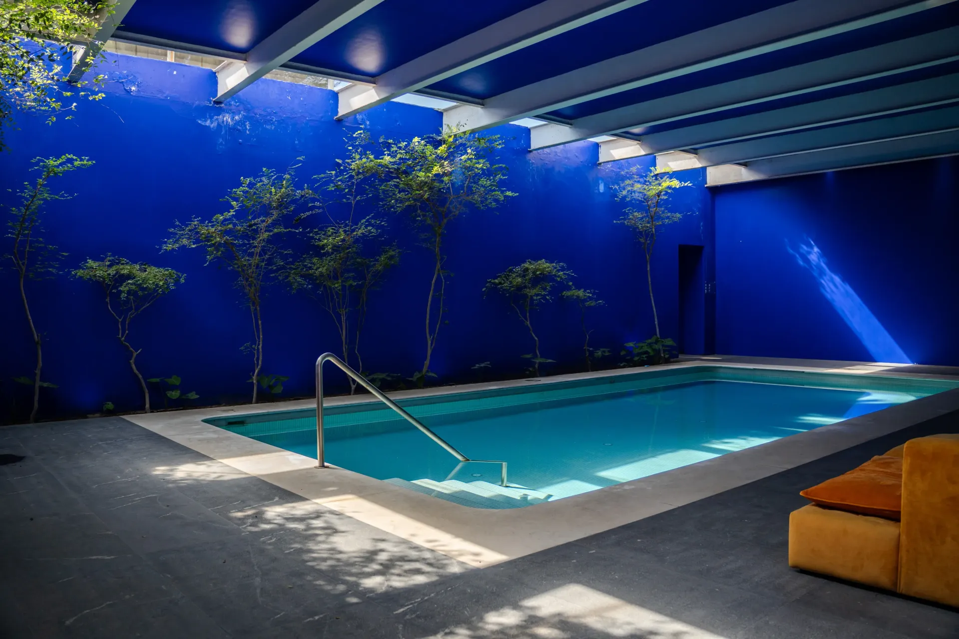 Piscina cubierta con paredes azules, vigas en el tragaluz y una barandilla metálica en las escaleras