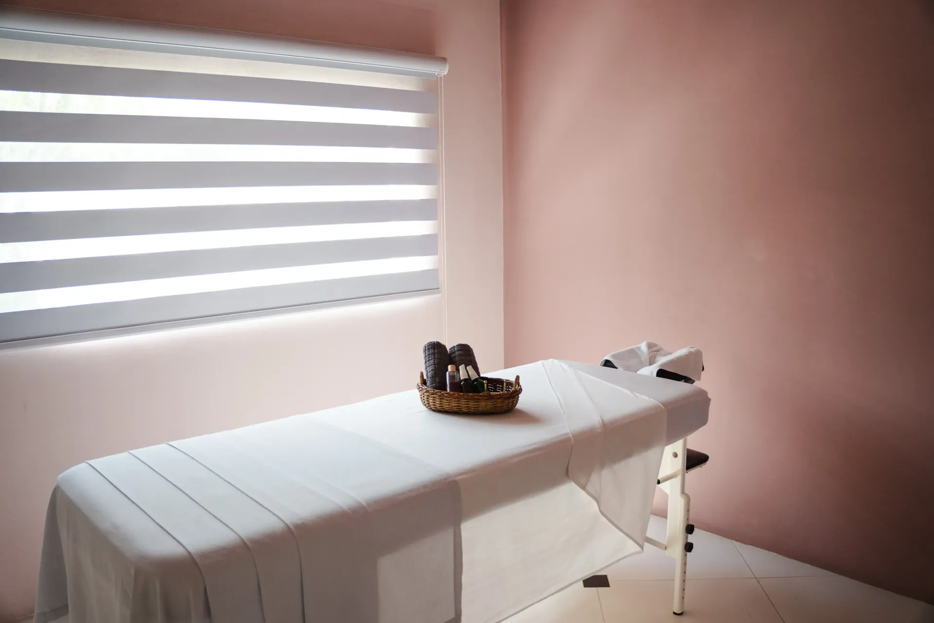 Sala de consulta con camilla, paredes rosas y una ventana con persianas venecianas