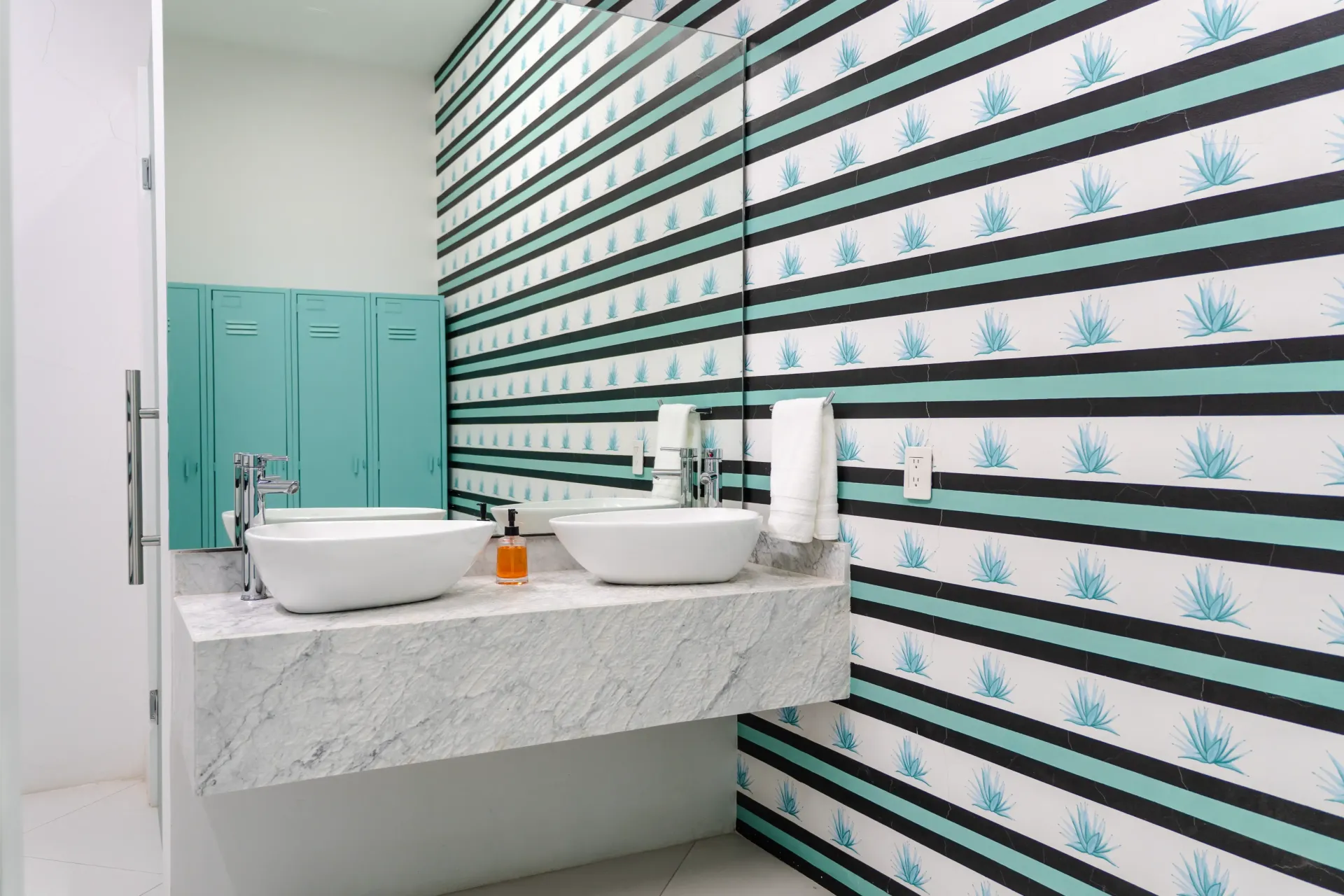 Baño moderno con papel pintado estampado, lavabo suspendido, espejo y taquillas verde azulado.