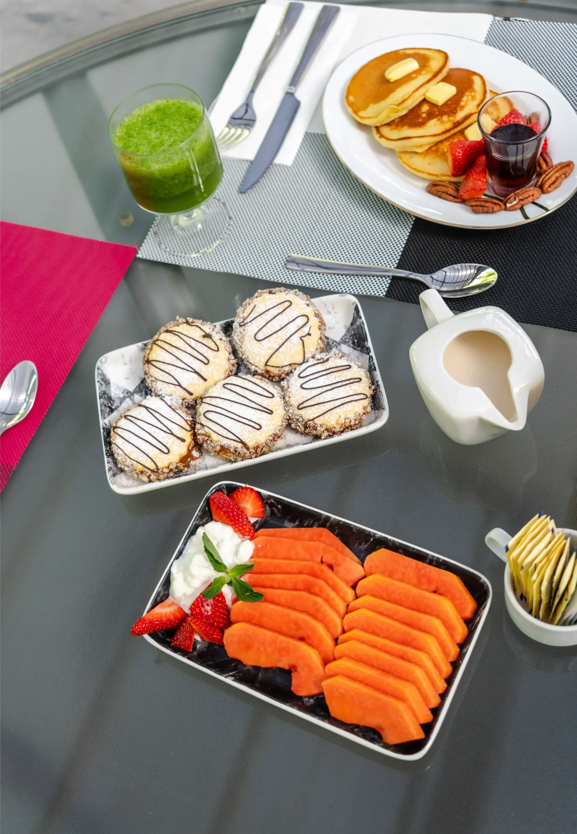 Mesa al aire libre con tortitas, sushi, bollería, zumo y café sobre una mesa de cristal en el patio