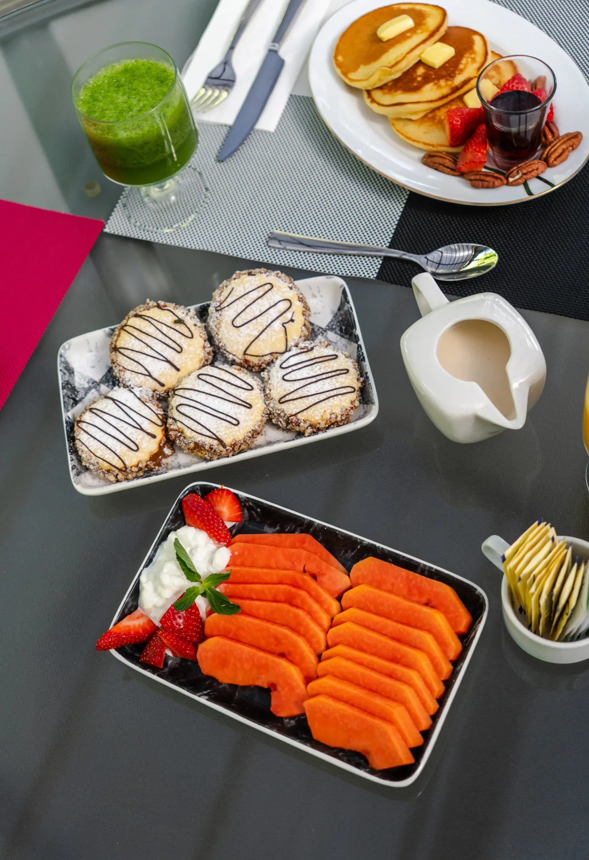 Desayuno con tortitas, gofres, sushi, fruta, un batido verde y café sobre una mesa