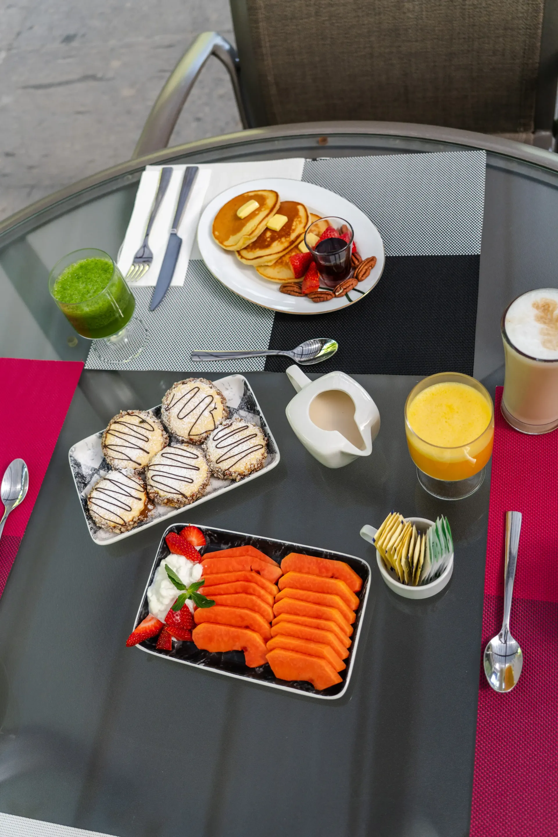 Mesa al aire libre con diversos platos de desayuno, fruta, bollería, zumo de naranja y café en una terraza