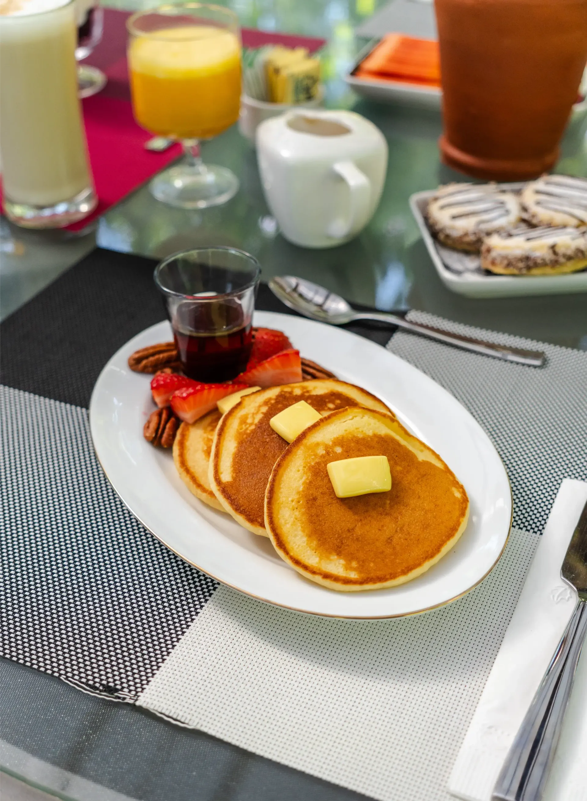 Plato de desayuno con tortitas, beicon y sirope sobre una mesa de comedor, con bebidas cerca