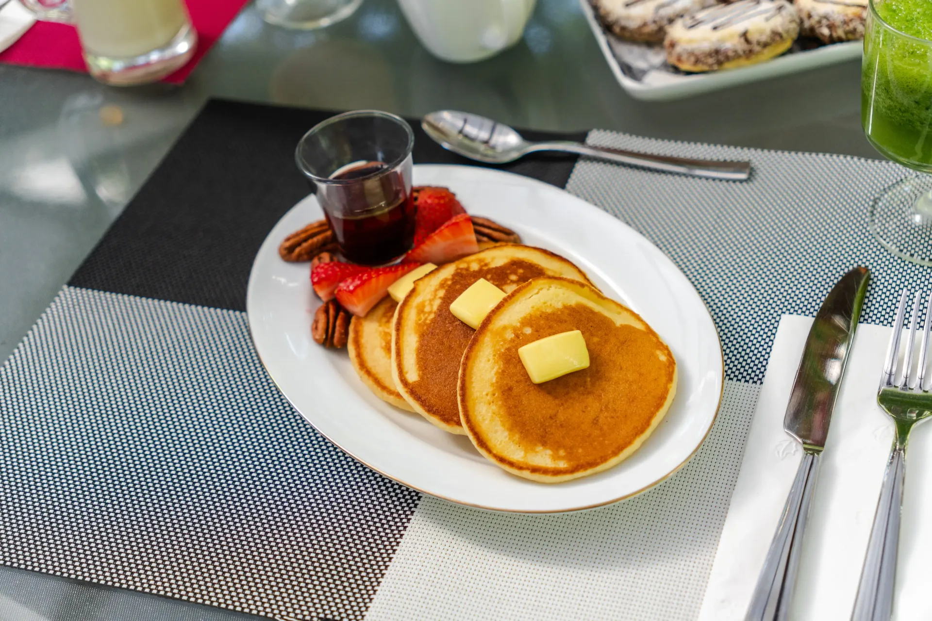Plato de desayuno con tortitas, sirope y una taza pequeña de café sobre una mesa