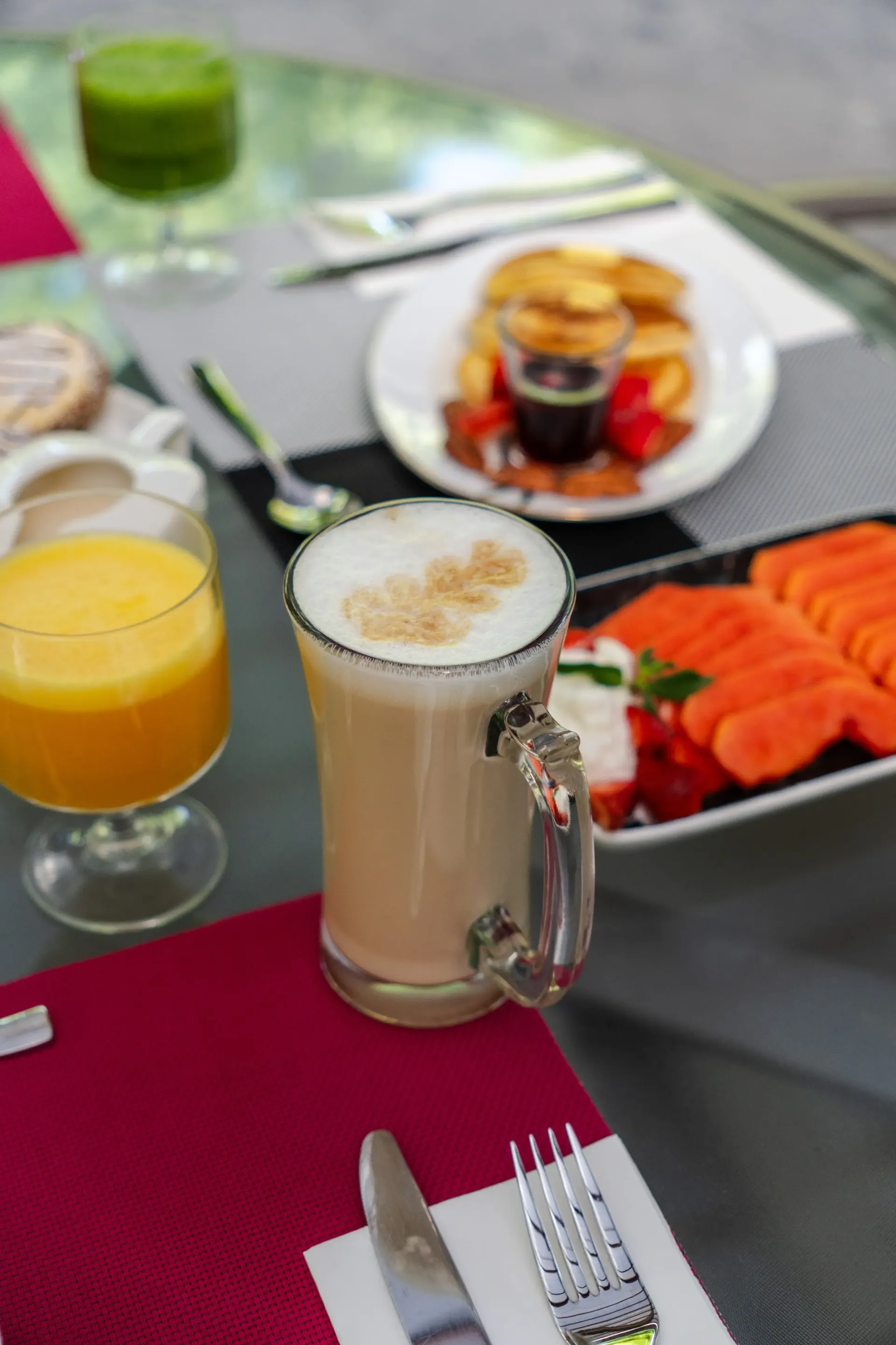 Mesa de desayuno en un patio, con zumo de naranja, café y un plato de fruta y bollería