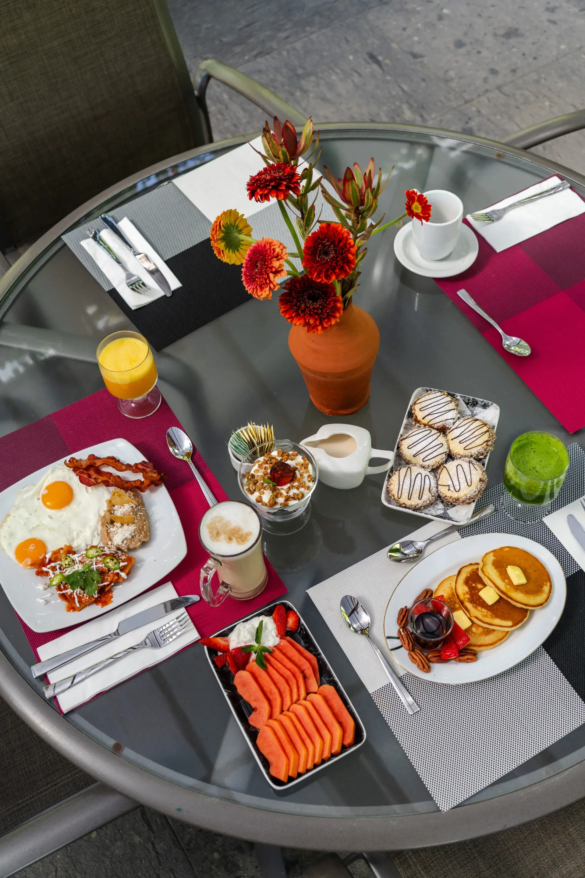 Mesa de patio al aire libre con sushi, platillos pequeños, flores y bebidas sobre una superficie de vidrio
