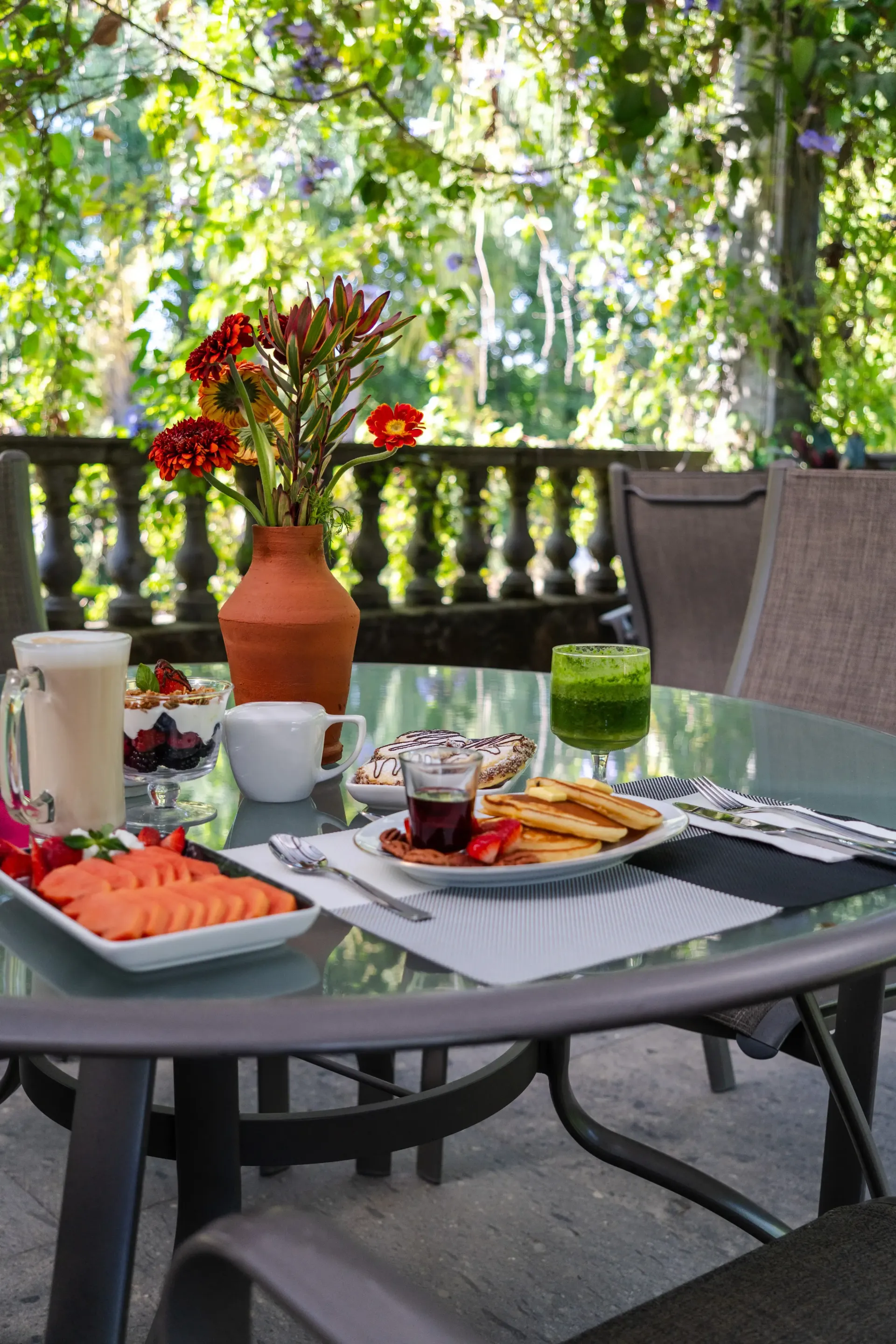 Mesa de exterior con té, pasteles, salmón y flores, con vistas a una exuberante vegetación