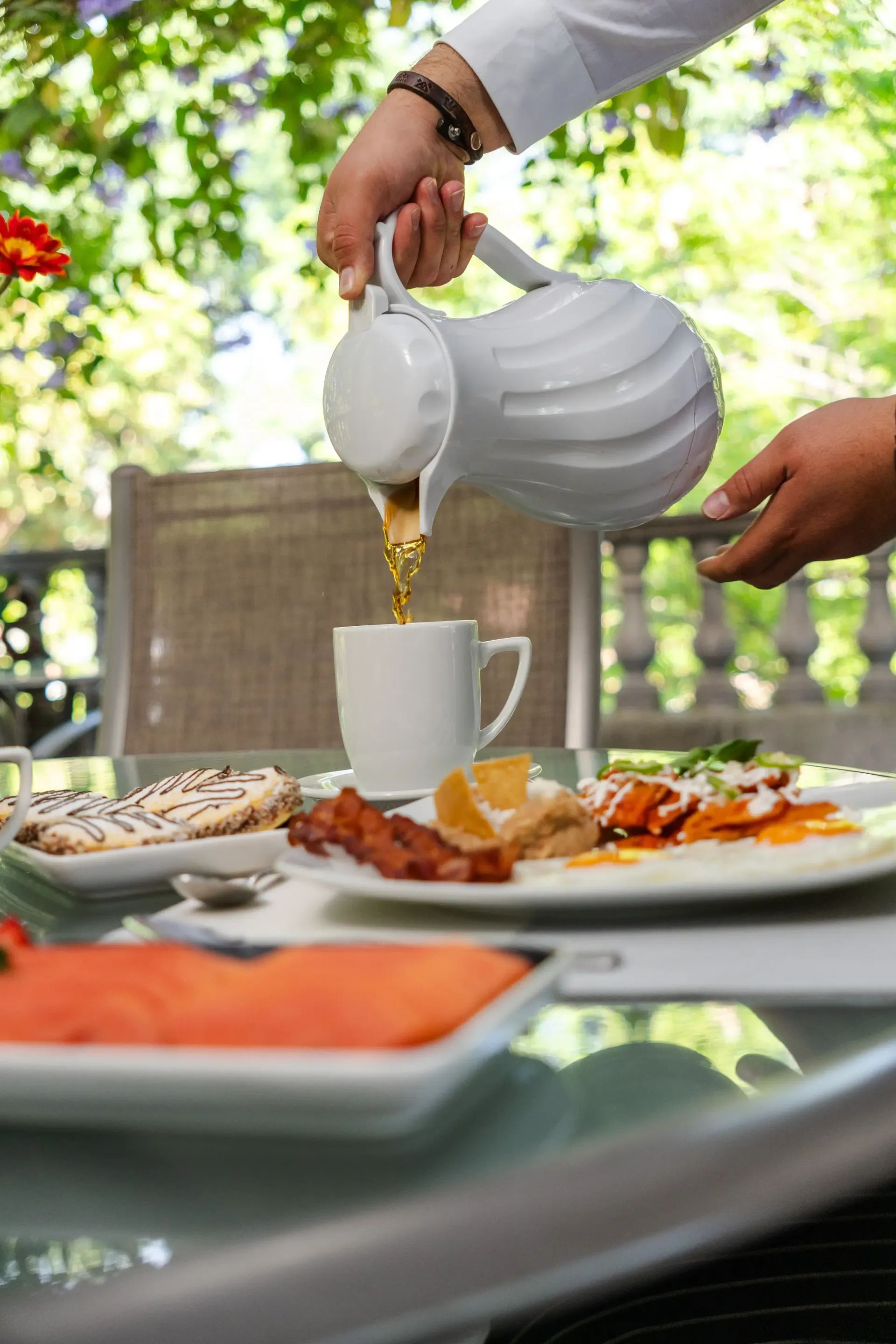 Té sirviéndose en una taza blanca en una mesa al aire libre con platos de comida.