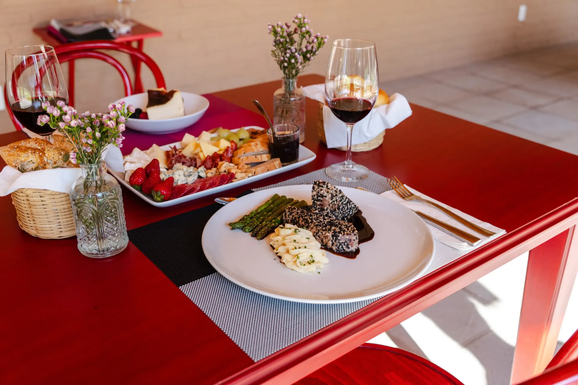 Mesa roja con un plato servido, copas de vino y una bandeja en un comedor luminoso
