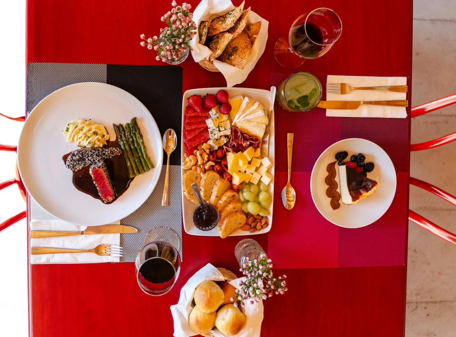 Juego de mesa rojo con una variedad de postres servidos en platos, frutos rojos y tazas dispuestos para una comida.