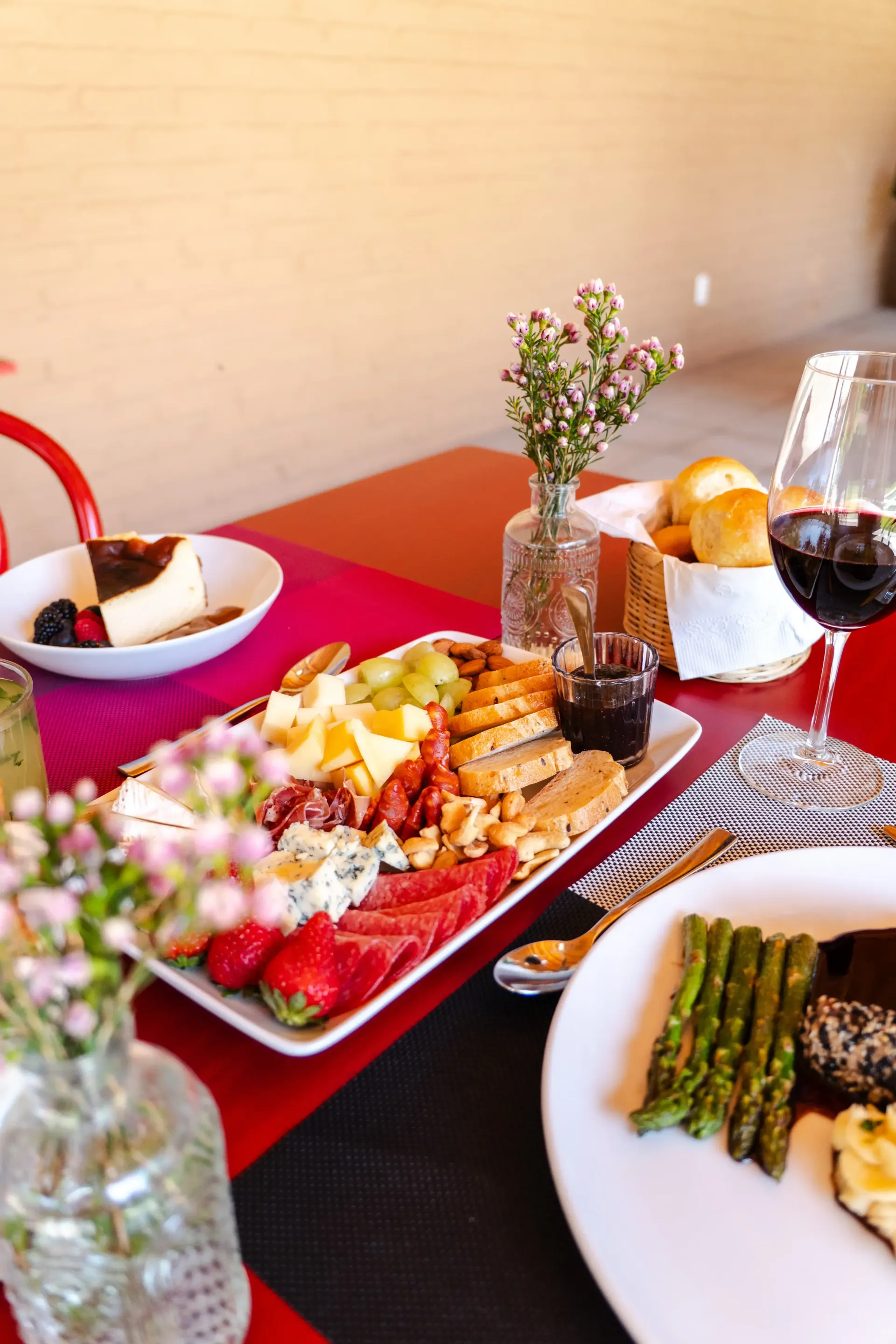 Elegante mesa de cena con mantel rojo, vino, bandejas de aperitivos y espárragos en platos blancos