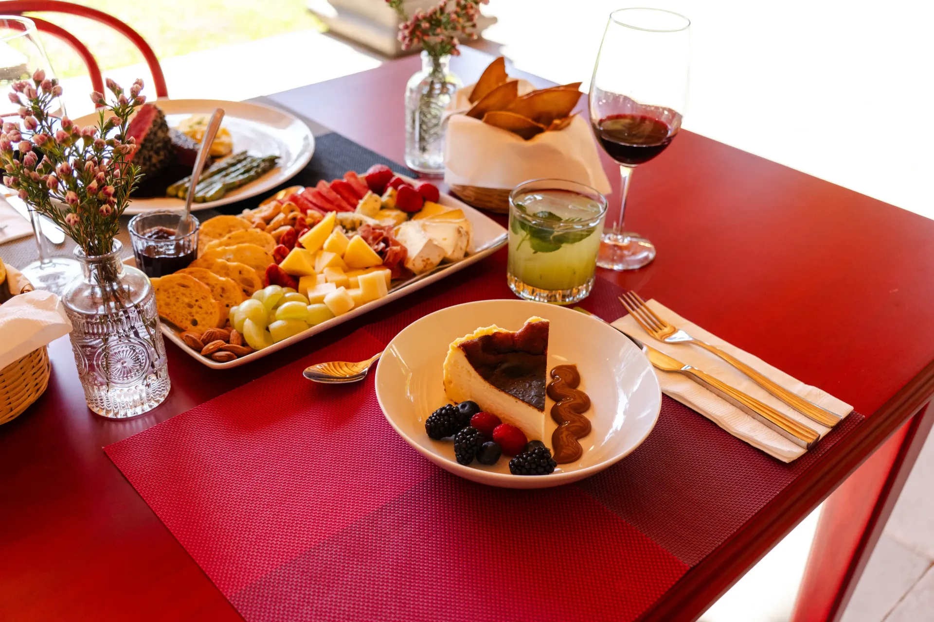 Mesa de comedor roja con platos de comida, copas de vino y cubiertos, preparada para servir una comida.