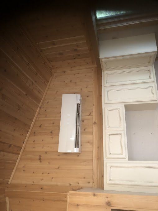 White air conditioning unit on a wooden wall. Beige cabinets are to the right.