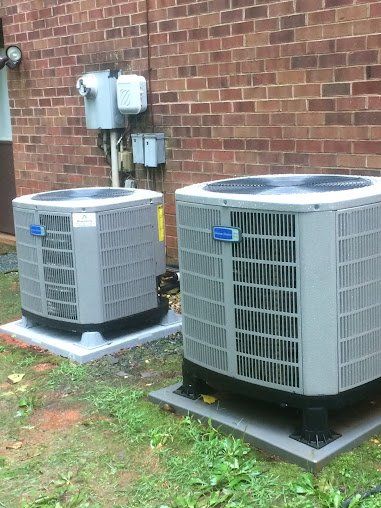 Two air conditioning units on concrete pads next to a brick building.