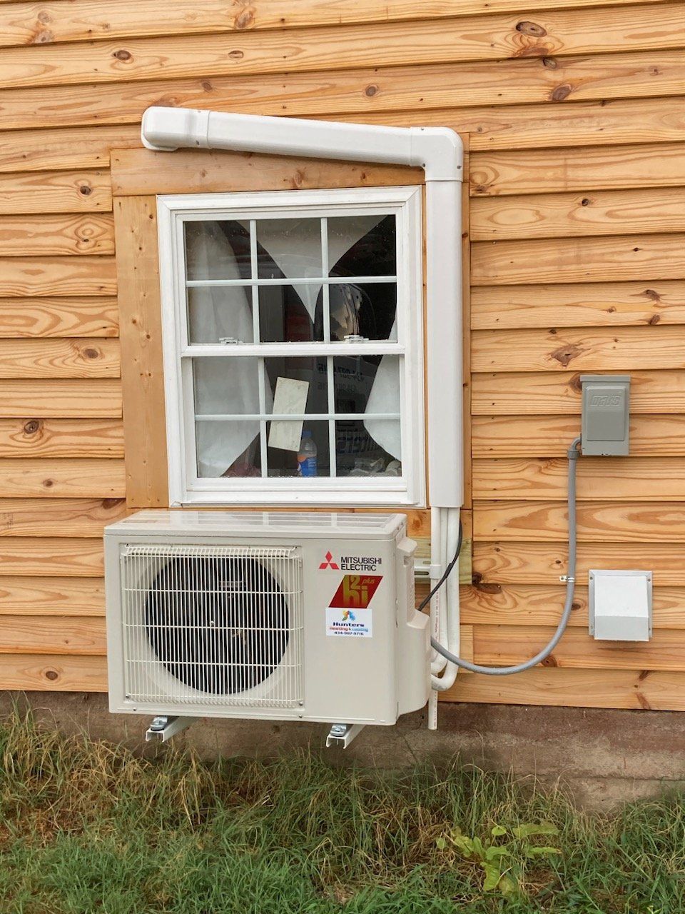 Exterior view of a window with an air conditioning unit below, white conduit, and a small electrical box.