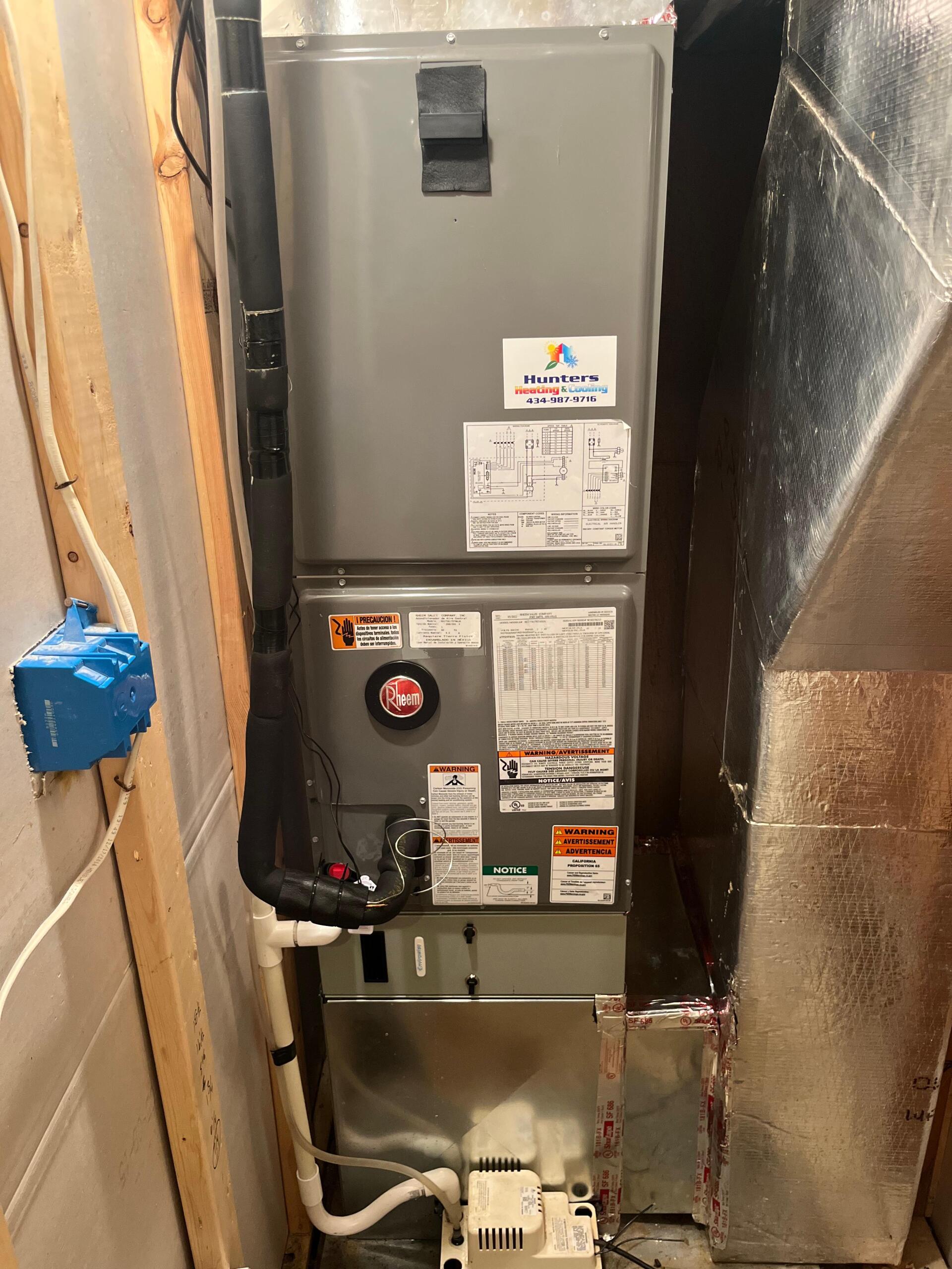 Furnace unit in a utility room, silver and gray with labels and ductwork.