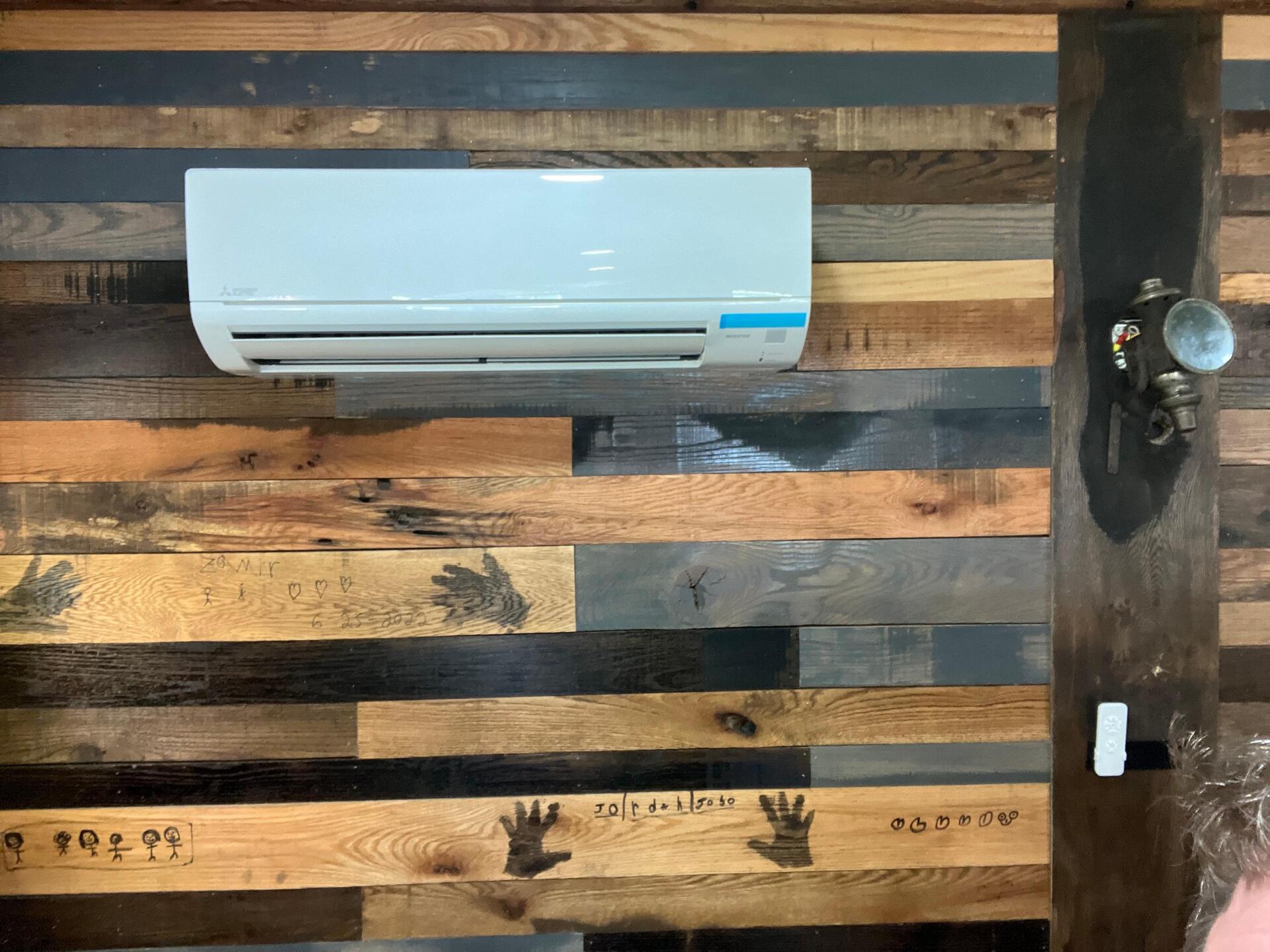 Air conditioner mounted on a rustic wooden wall with handprints.