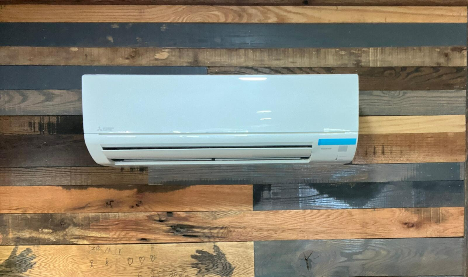 Air conditioner mounted on a rustic wood plank wall. The unit is white with blue accents.