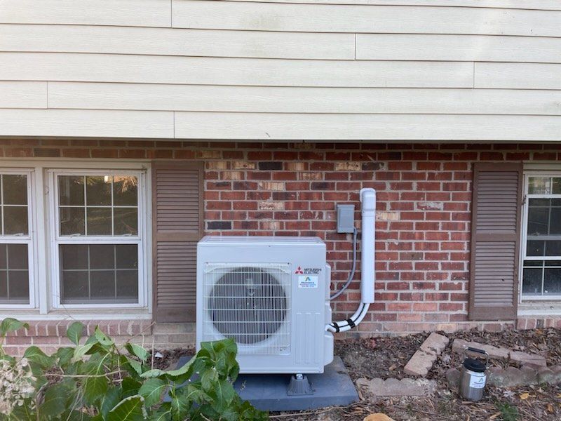 Mitsubishi heat pump unit installed outside a brick home with windows.
