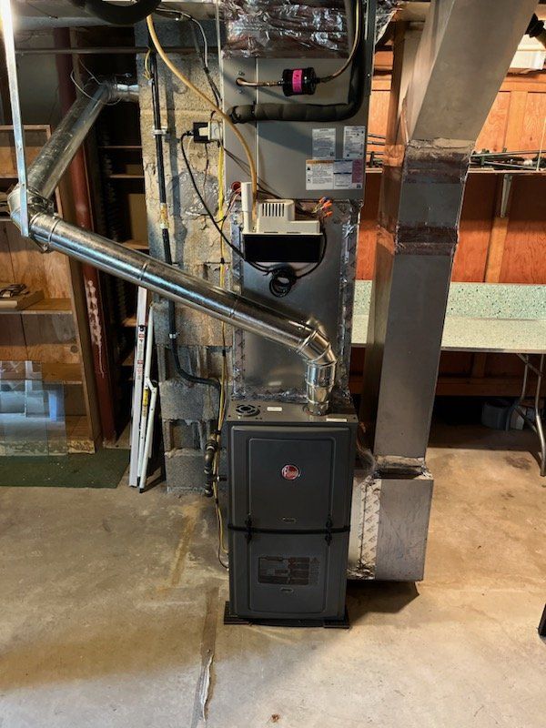 A Rheem furnace installed in a basement, with silver ductwork and vent pipes.