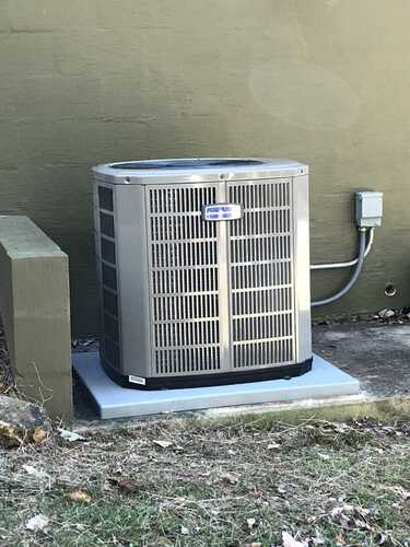 Air conditioning unit outside a building, set on a concrete pad, connected to a power source.