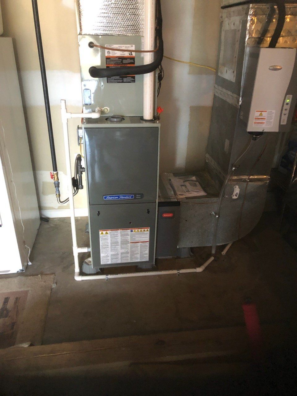 Furnace and HVAC system in a basement. Grey metal unit with ductwork, safety labels and piping.