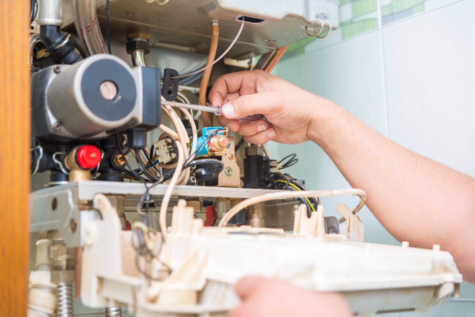 Person repairing a boiler, using a screwdriver, close-up view of the appliance's inner workings.