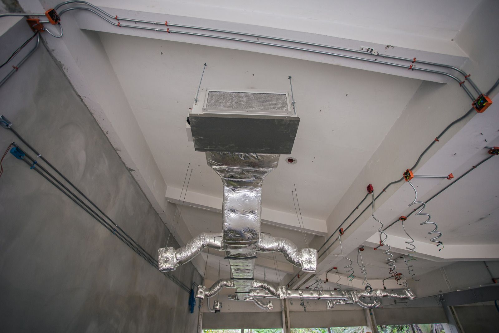 HVAC ductwork and electrical wiring on a concrete ceiling of a building under construction.
