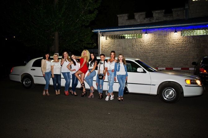 Group of people posing beside a white limousine at night outside a brick building.