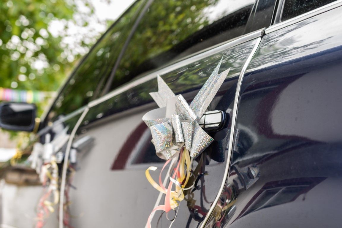Bouquet of flowers tied to the side mirror of a dark blue car on a street