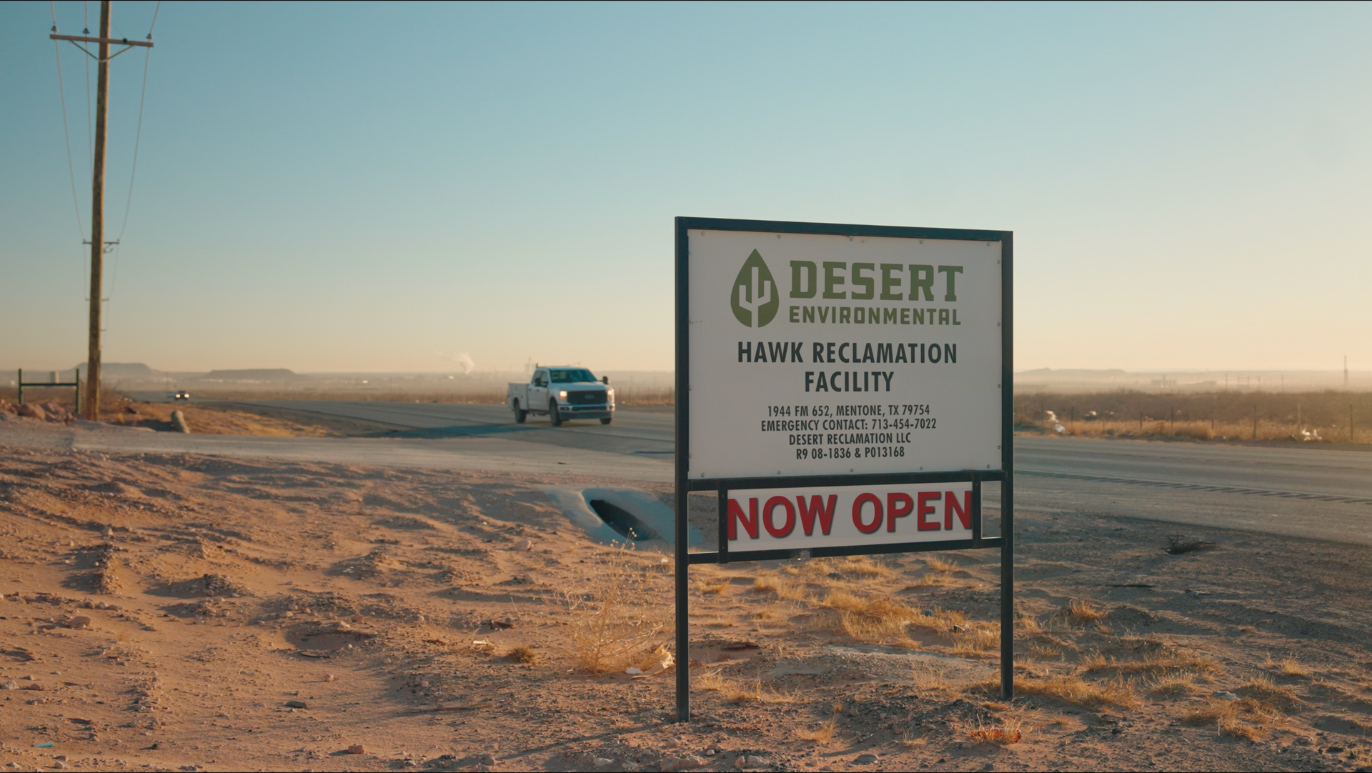 A white truck is driving down a desert road next to a sign that says 