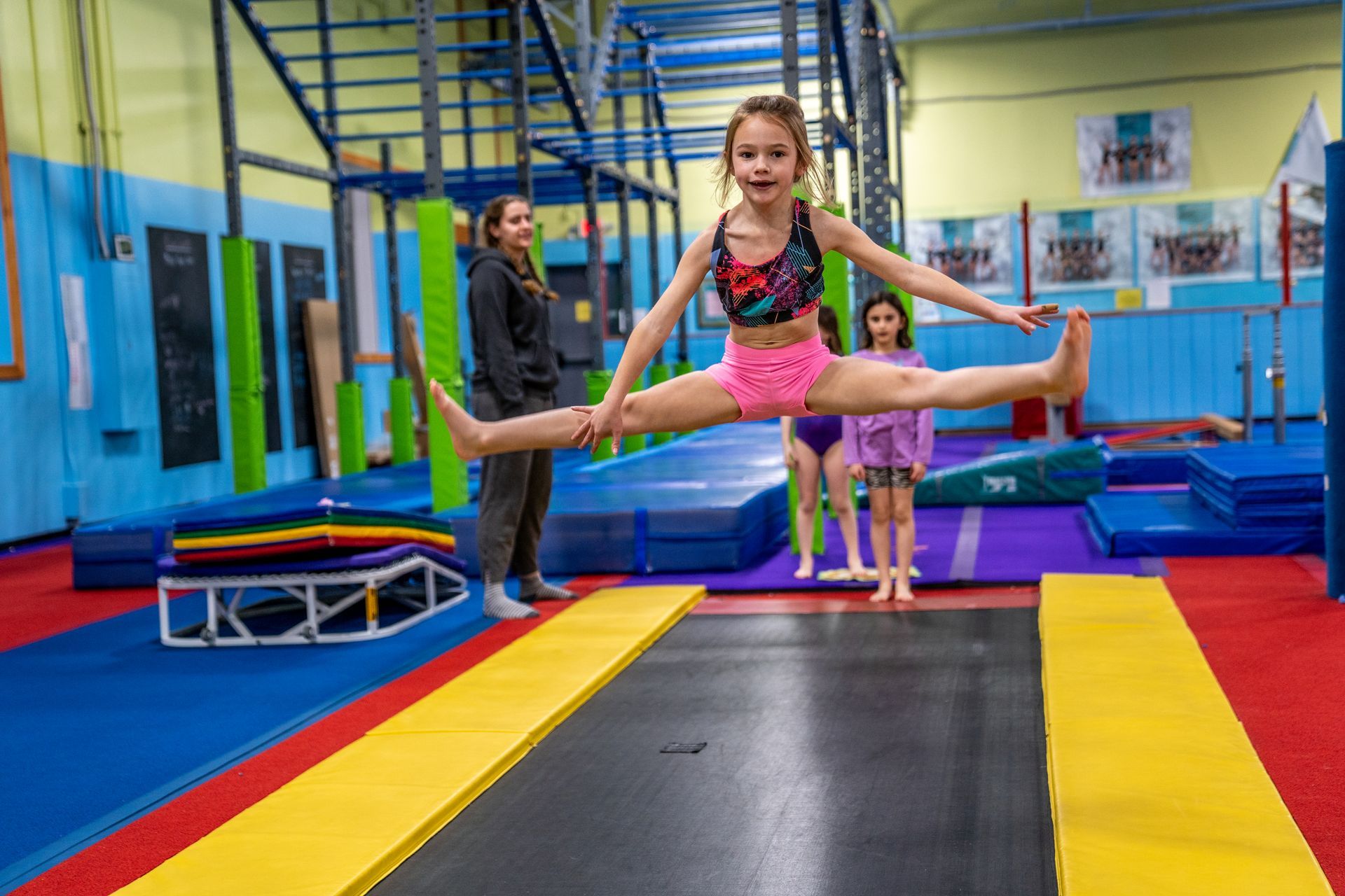 A young girl is doing a straddle jump on a trampoline in a gym.