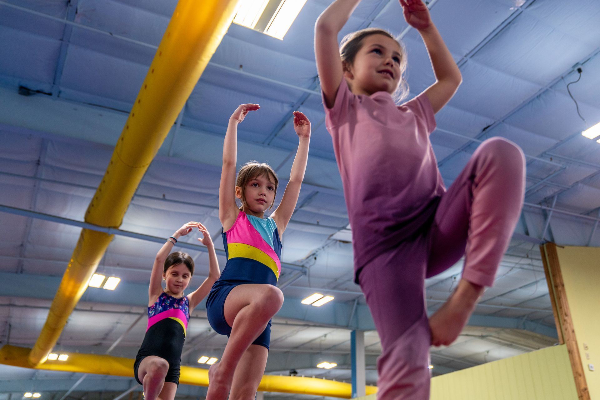 Three young girls are doing exercises on a balance beam in a gym.