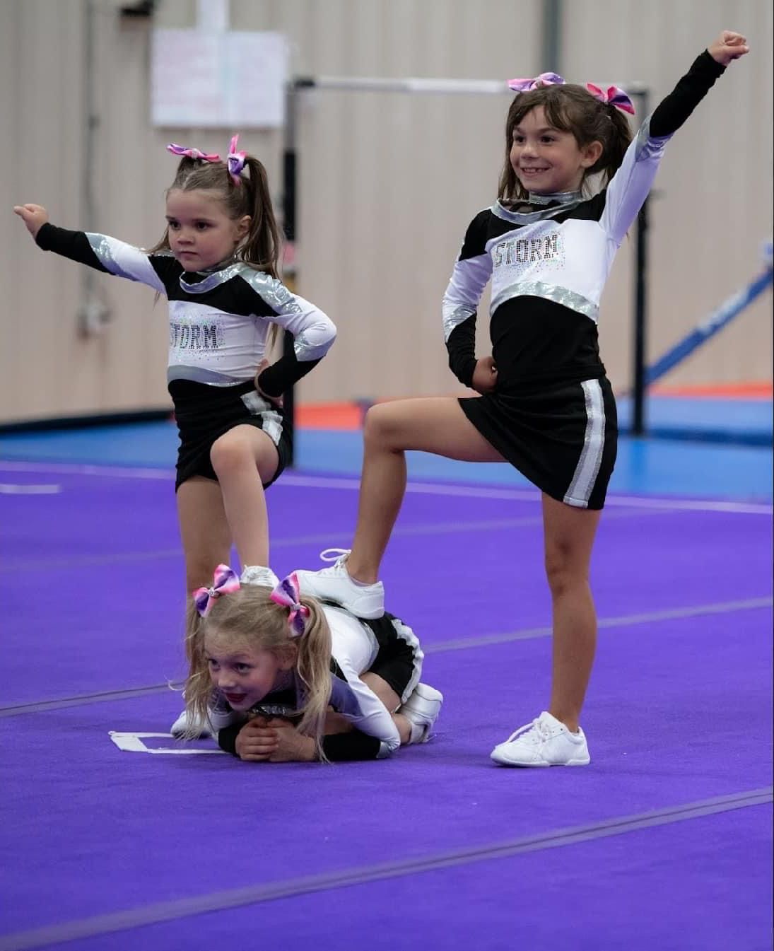 Three young cheerleaders are performing on a purple mat.