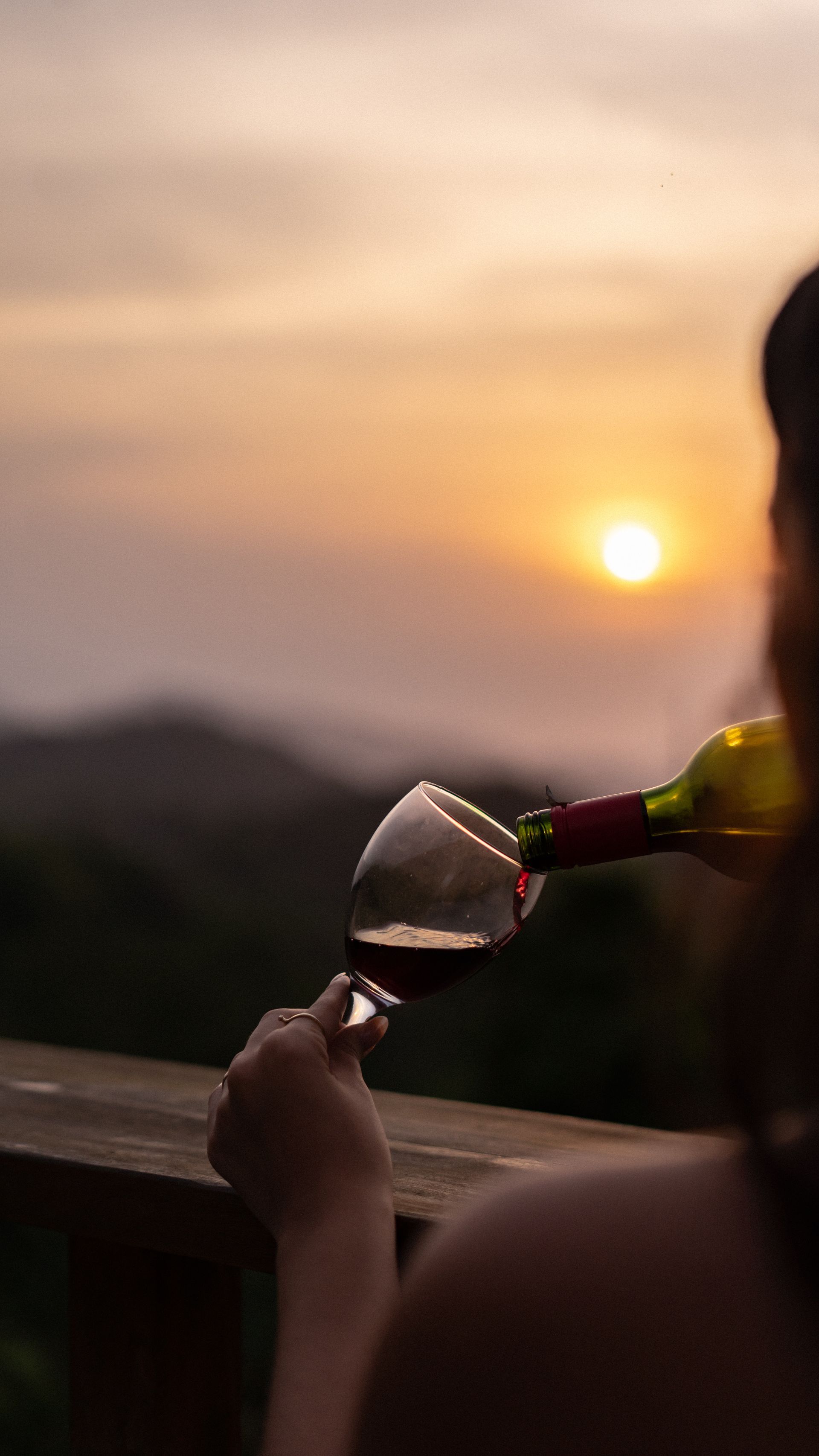 A woman is pouring wine into a glass at sunset.