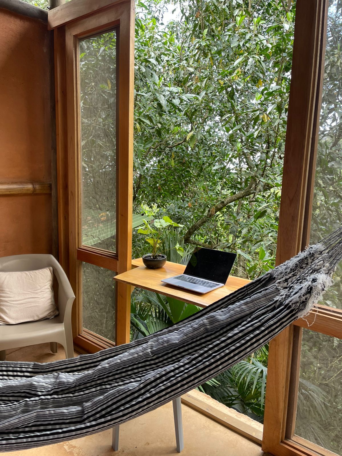 A hammock is sitting next to a desk with a laptop on it.