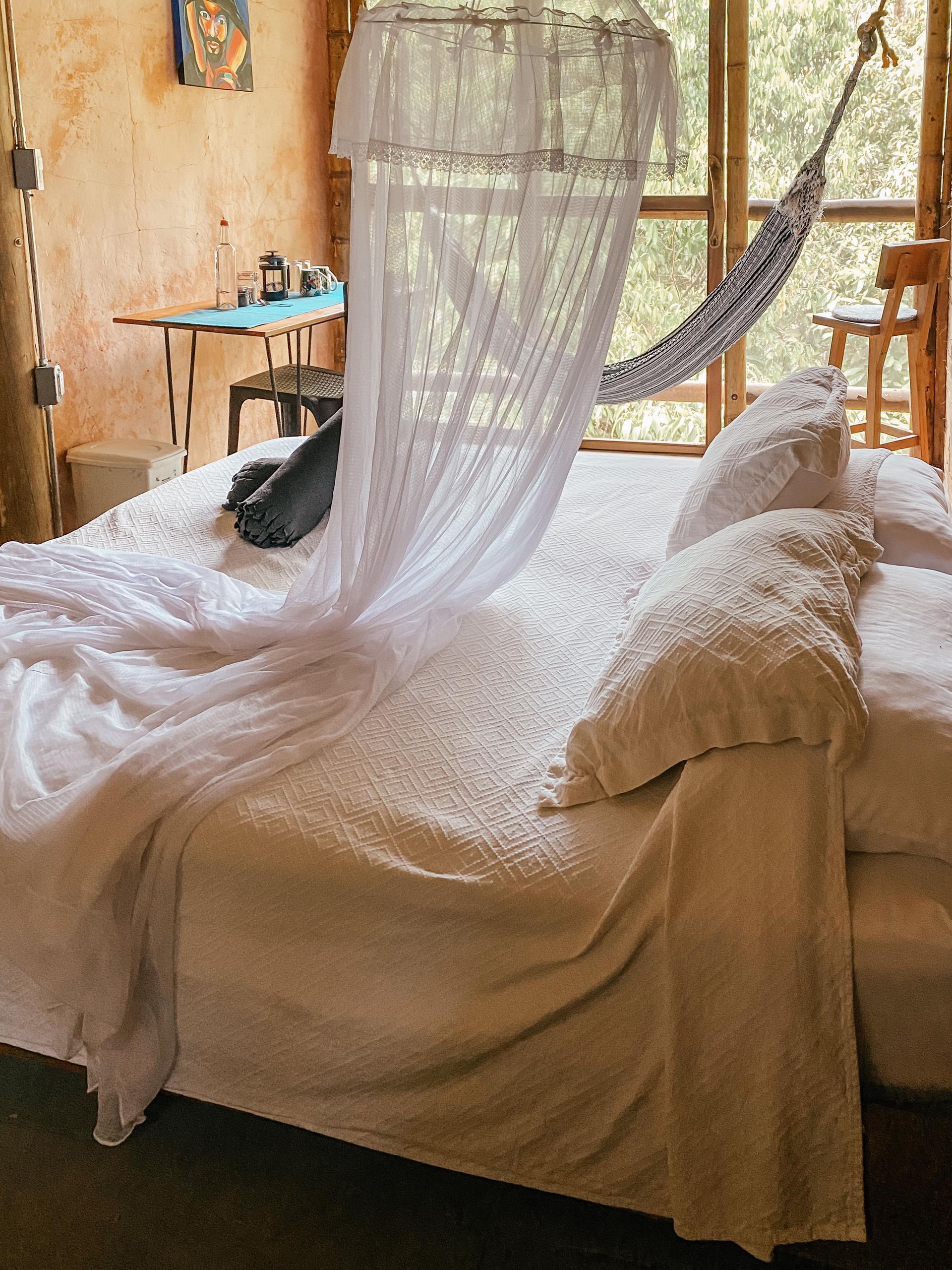 A bed with white sheets and a hammock hanging over it