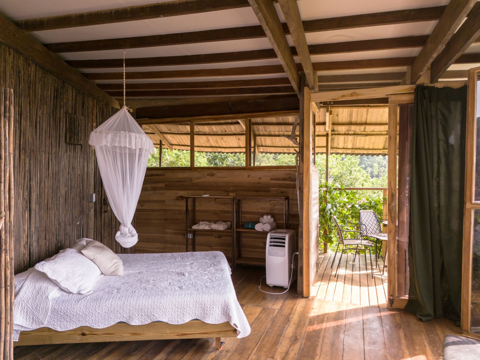A bedroom in a wooden house with a bed and mosquito net.