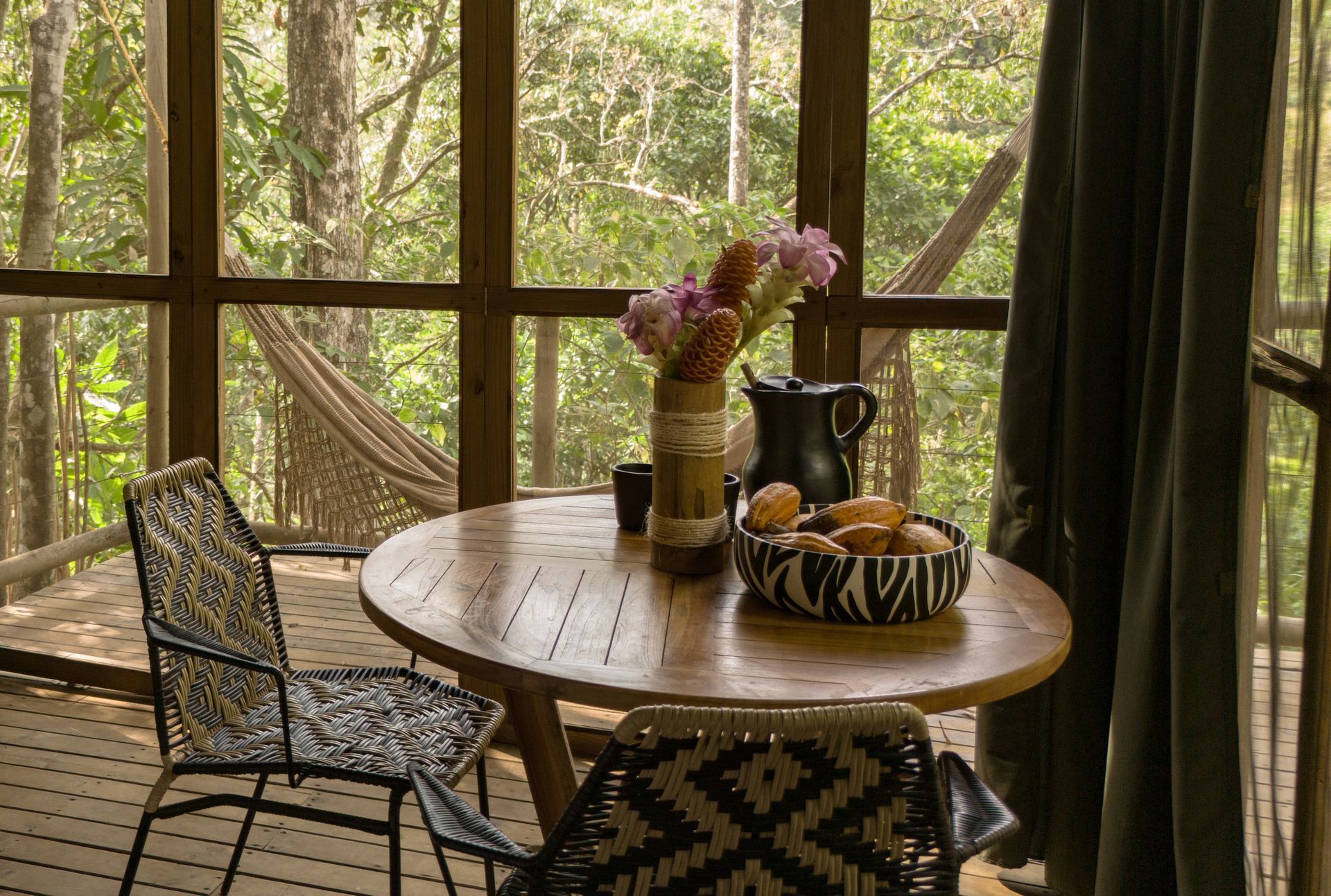 There is a table and chairs on the porch with a hammock in the background.