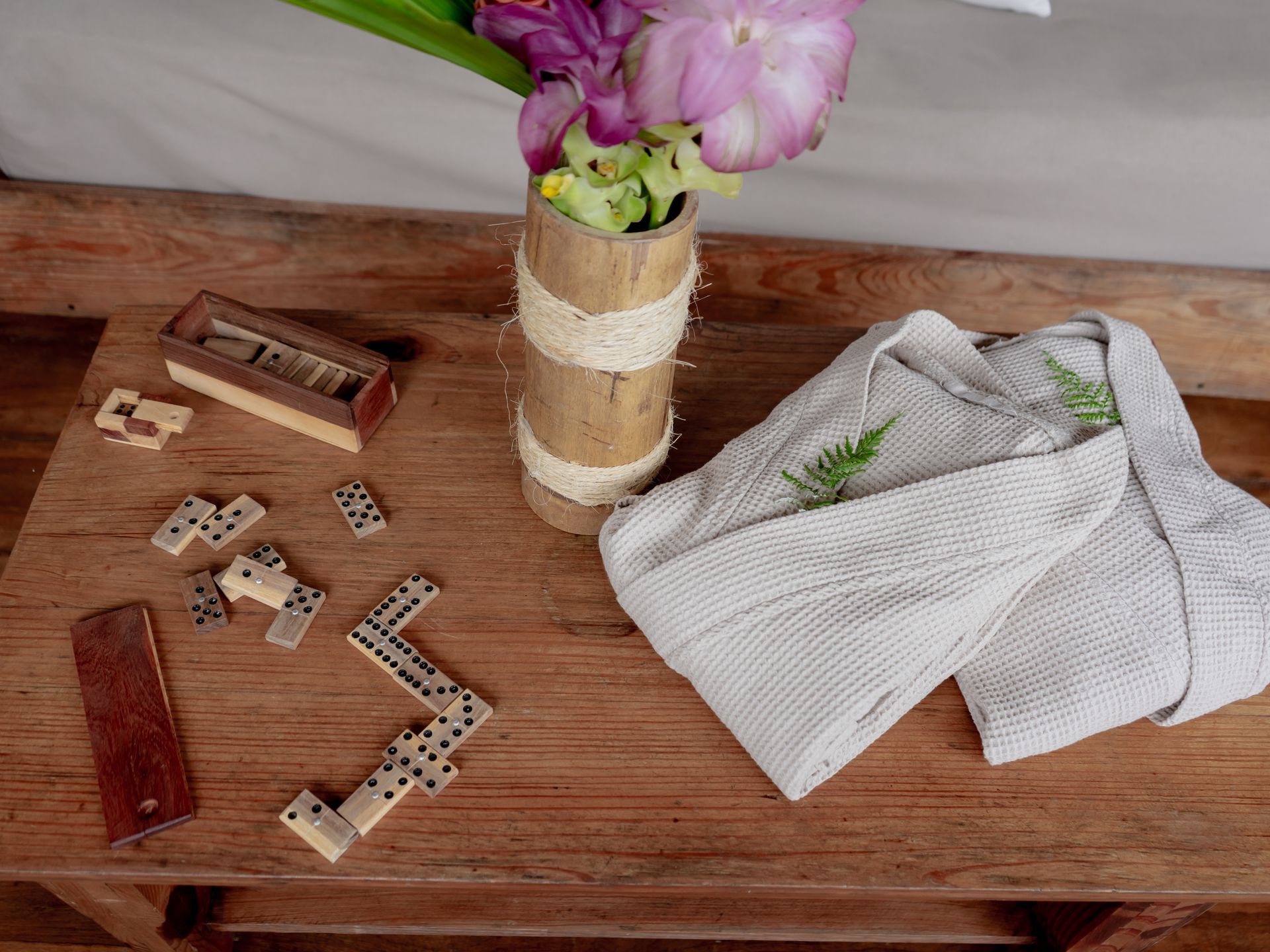 A wooden table with a vase of flowers and dominoes on it.