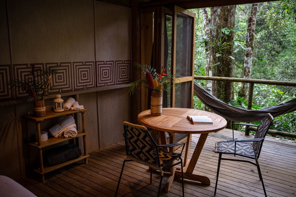 There is a table and chairs on the deck of a tree house.
