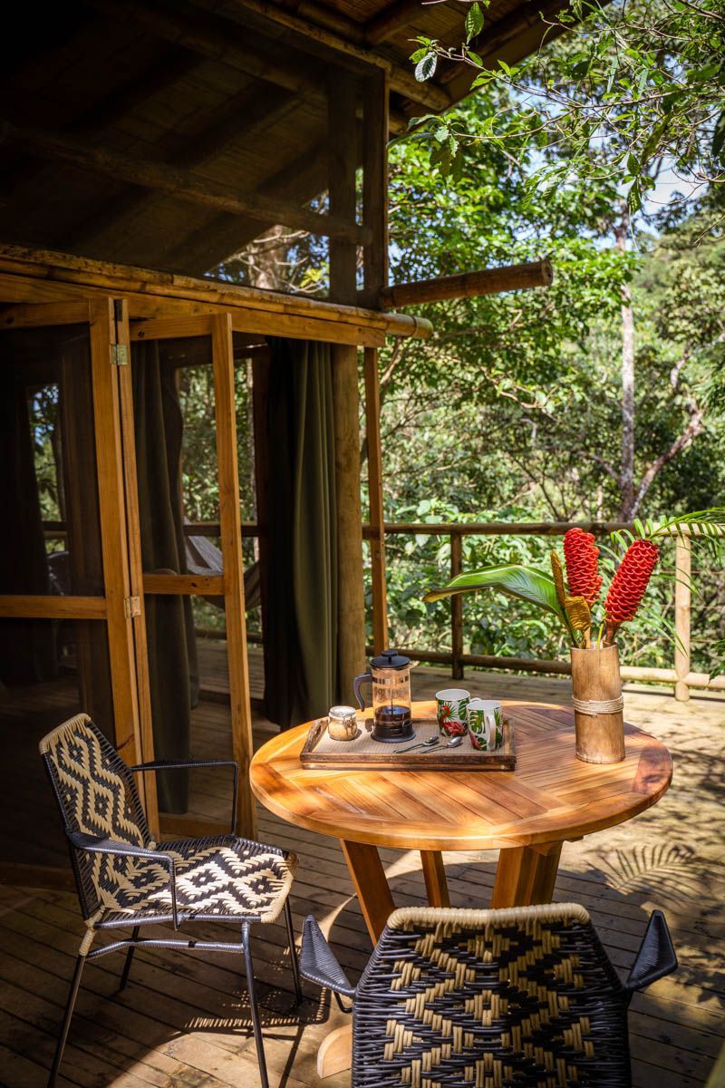 There is a table and chairs on the deck of a tree house.