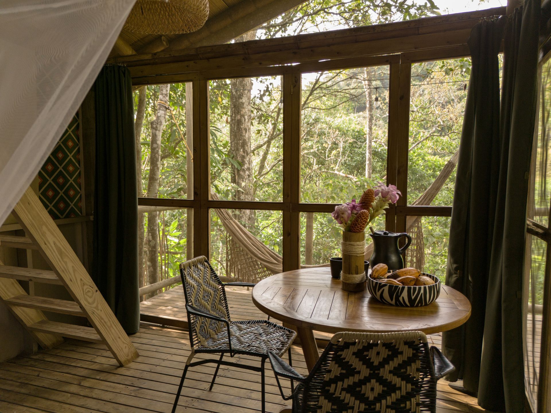 There is a table and chairs in the room with a view of the trees.