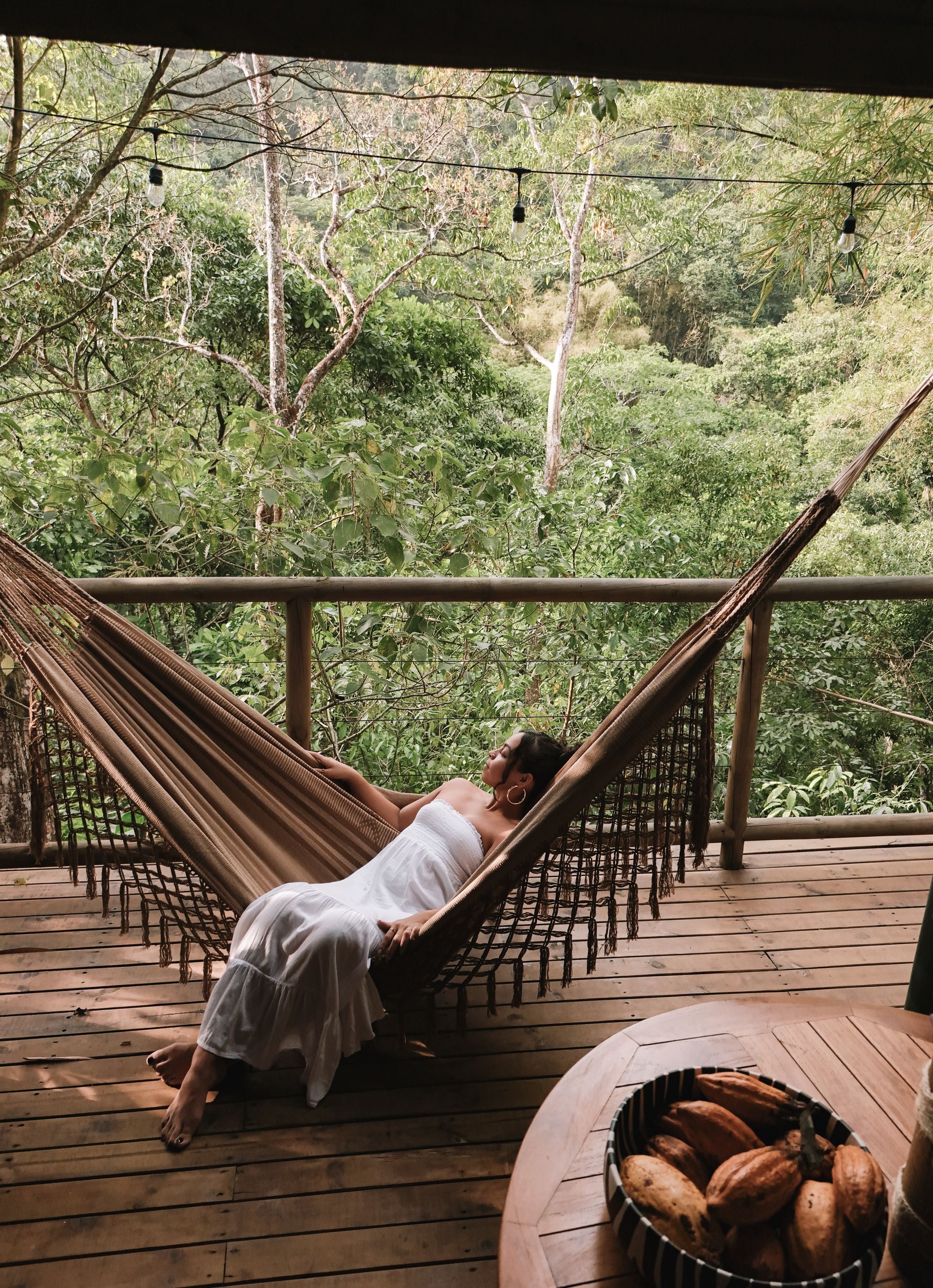 A woman is laying in a hammock on a deck.