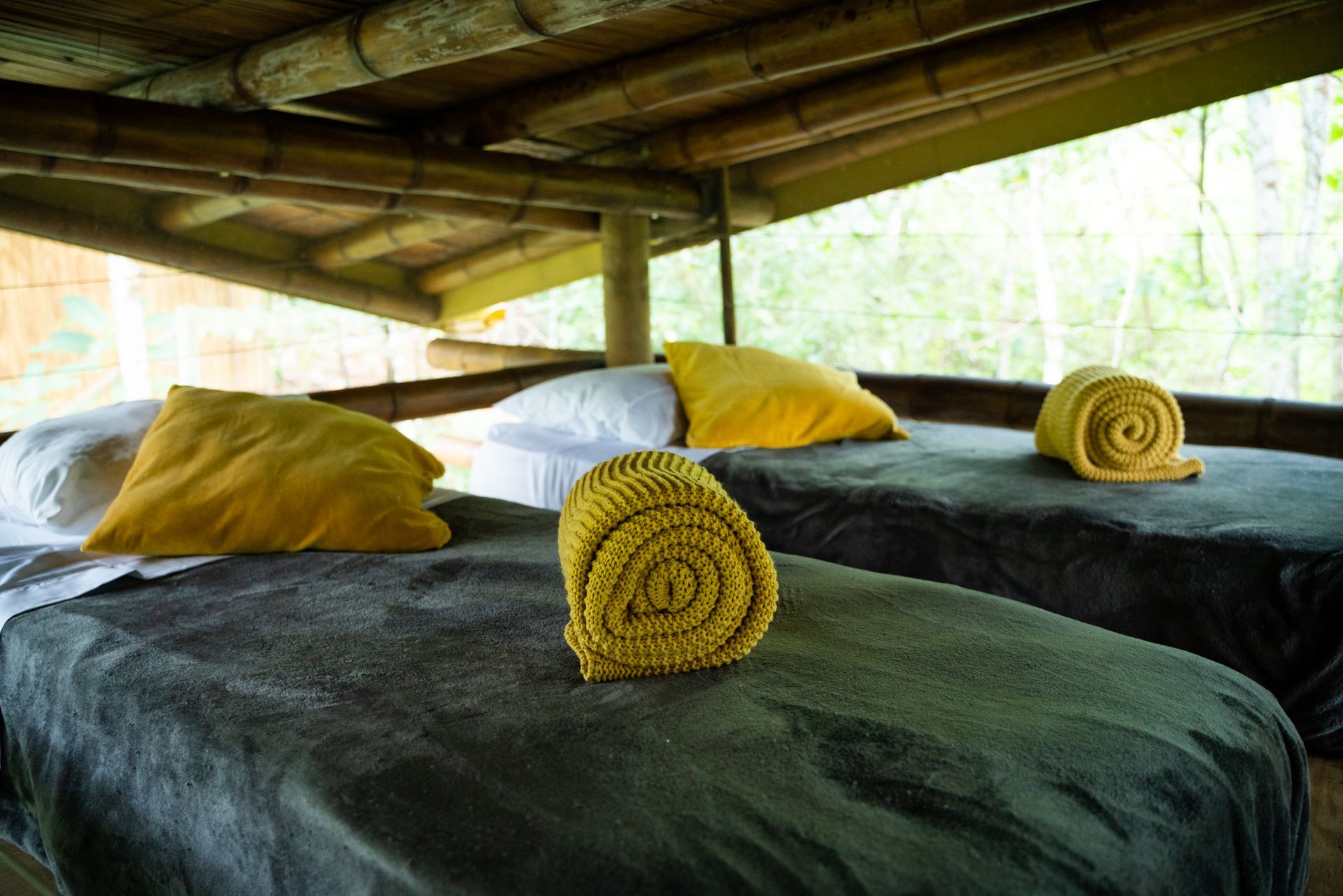 Two beds with yellow pillows and towels on them in a room with a bamboo roof.