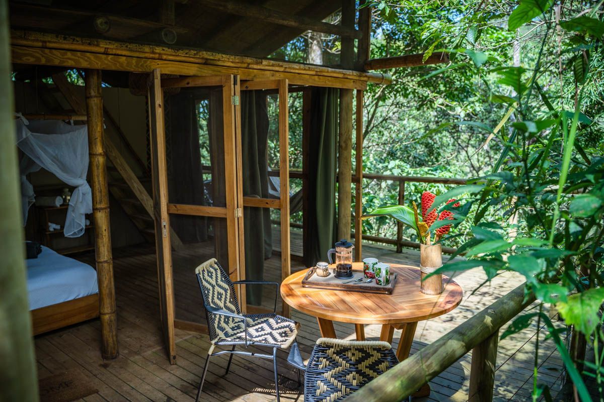 There is a table and chairs on the deck of a tree house.