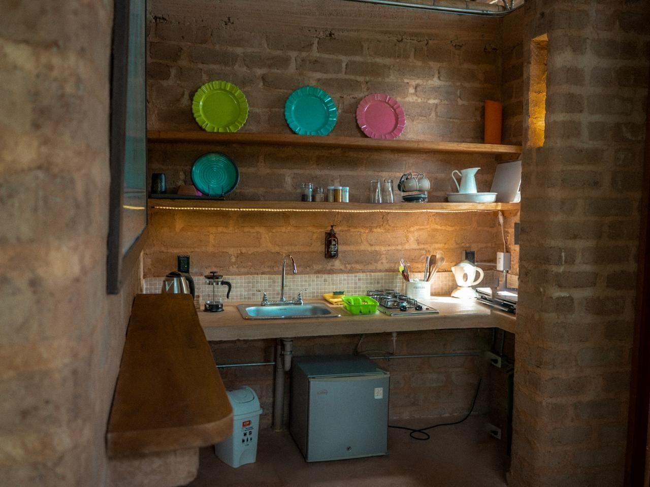 A kitchen with a sink , shelves , and plates on the wall.