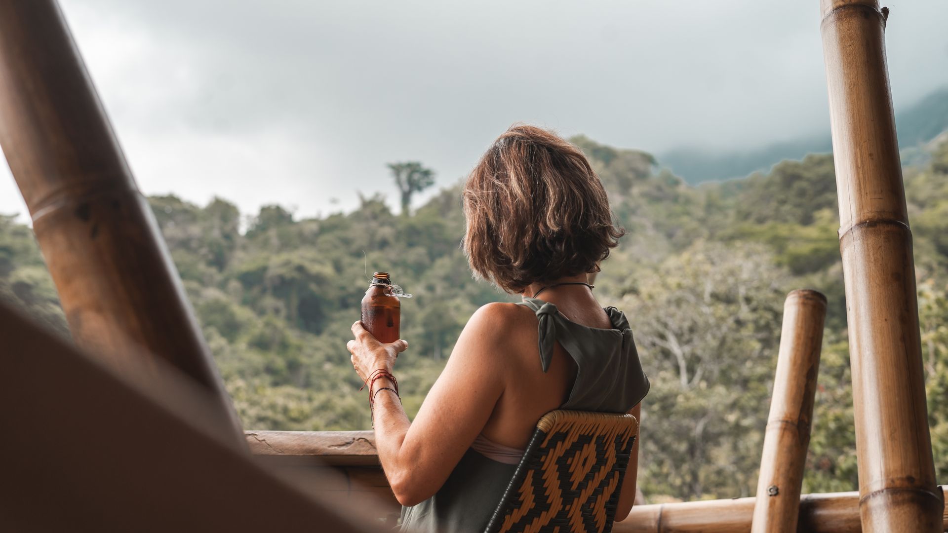 A woman is sitting on a balcony looking out over a forest.