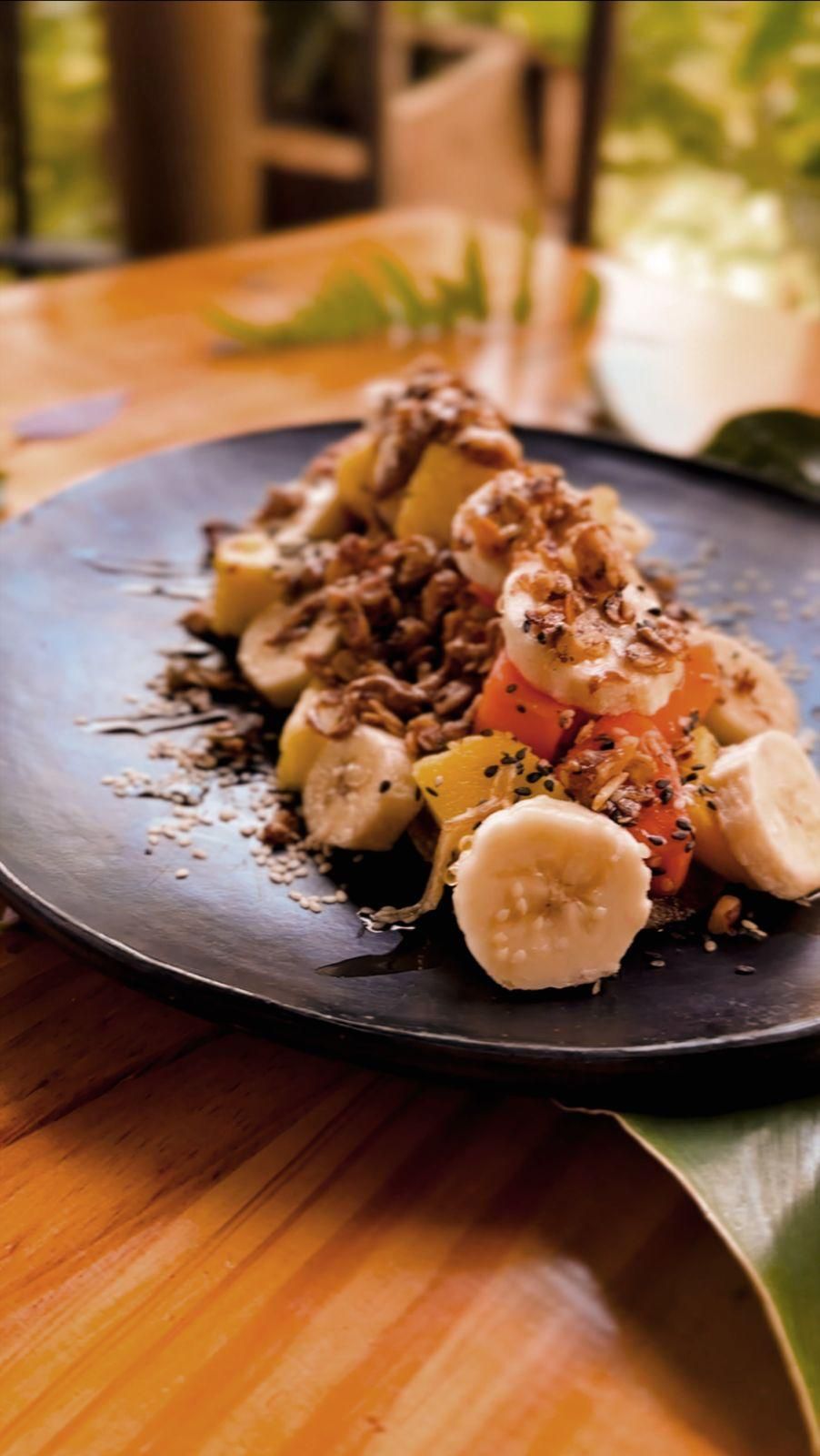A black plate topped with bananas and nuts on a wooden table.