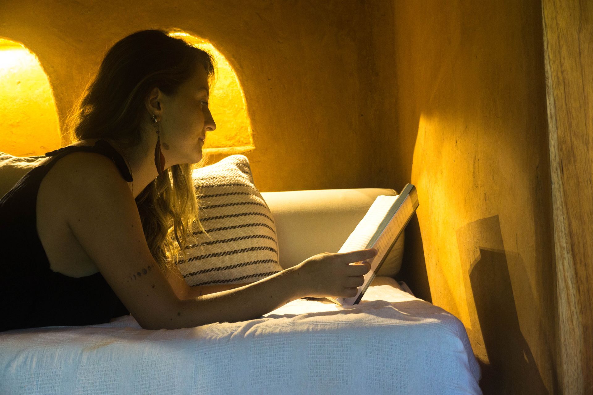 A woman is laying on a couch reading a book.